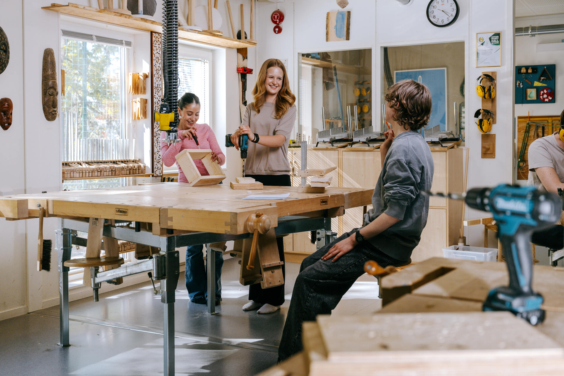 Elever arbetar tillsammans i en slöjdsal på Ekens skola i Hammarby Sjöstad, där de borrar och monterar trädetaljer runt ett arbetsbord i en ljus och välutrustad undervisningsmiljö.