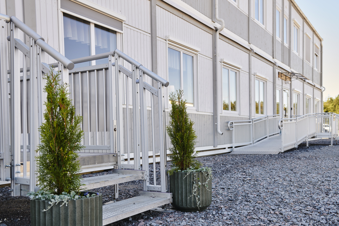 Exteriör av kontorsmoduler från Expandia med entré, trappa och ramp med räcken. Fasaden är ljus med flera fönster, och gångytor leder fram till ingångarna. Bilden är tagen vid Alviks trafik i Luleå.