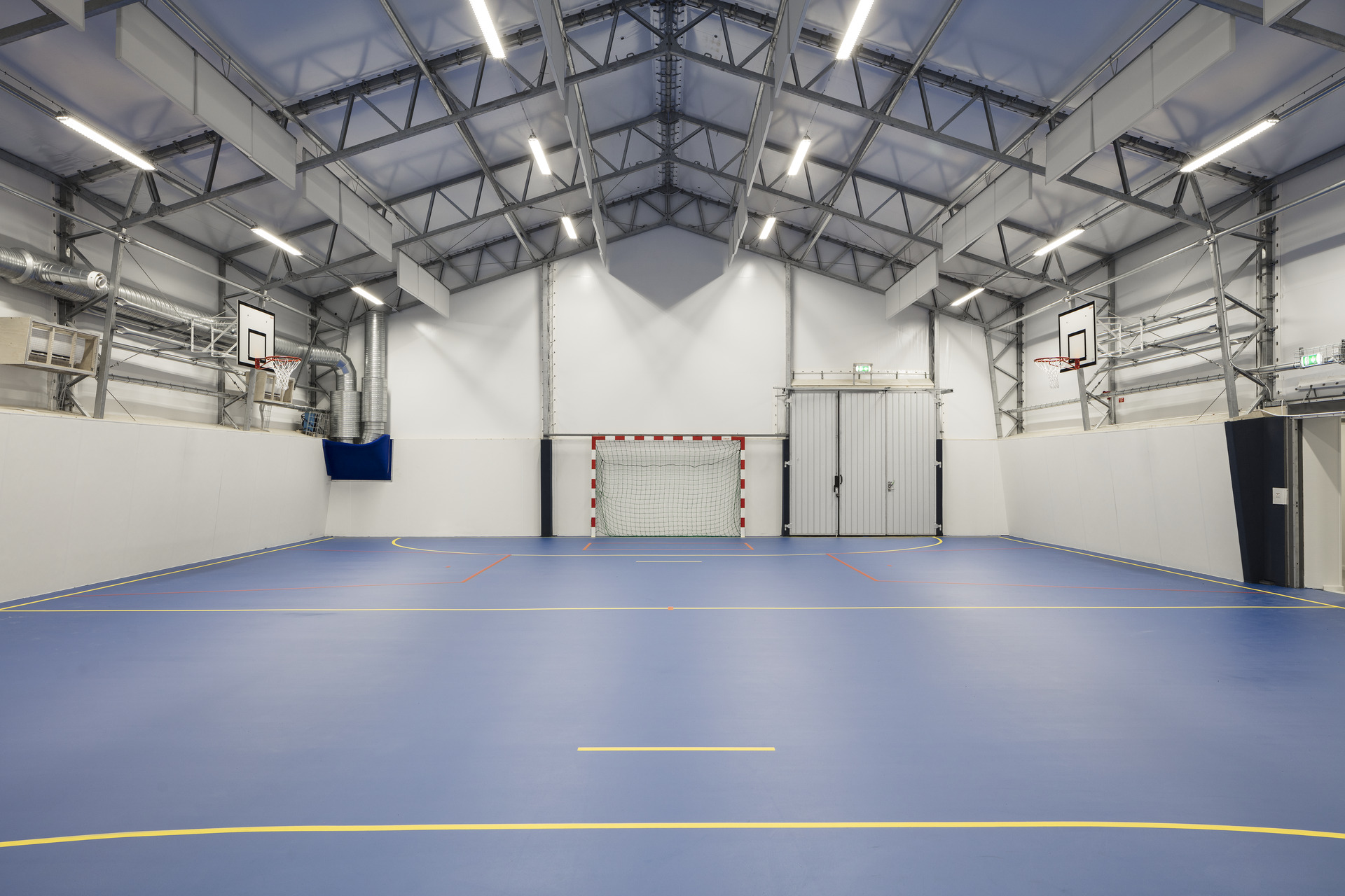 Invändig idrottshall i skolmodullösning från Expandia, med blå sportgolv, målbur, basketkorgar, högt i tak och jämn belysning.