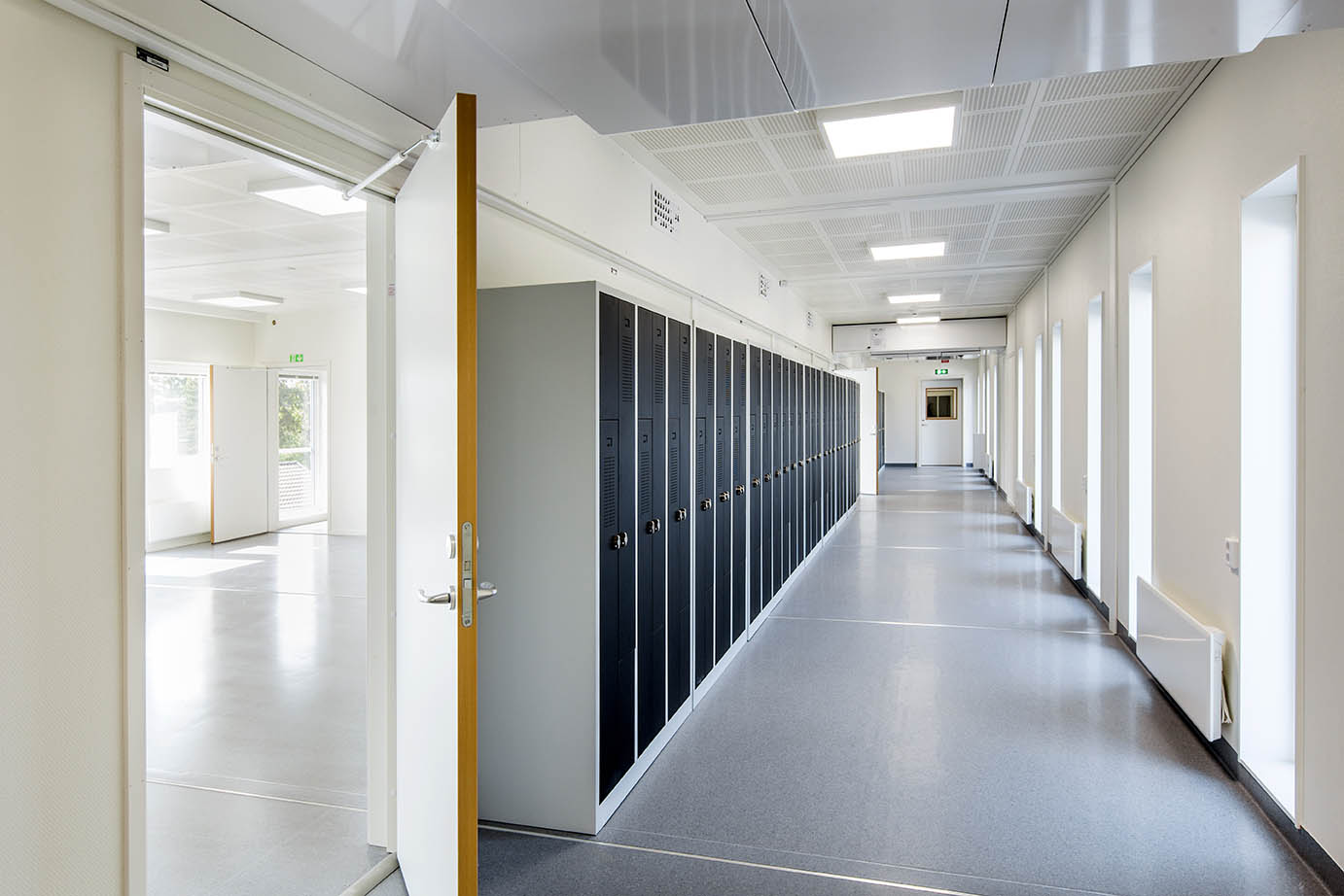 Ljus korridor i Falkbergsskolans modullösning i Tullinge med skåpförvaring längs ena väggen, stora fönster och öppningar mot klassrum – en modern och funktionell modullösning från Expandia.