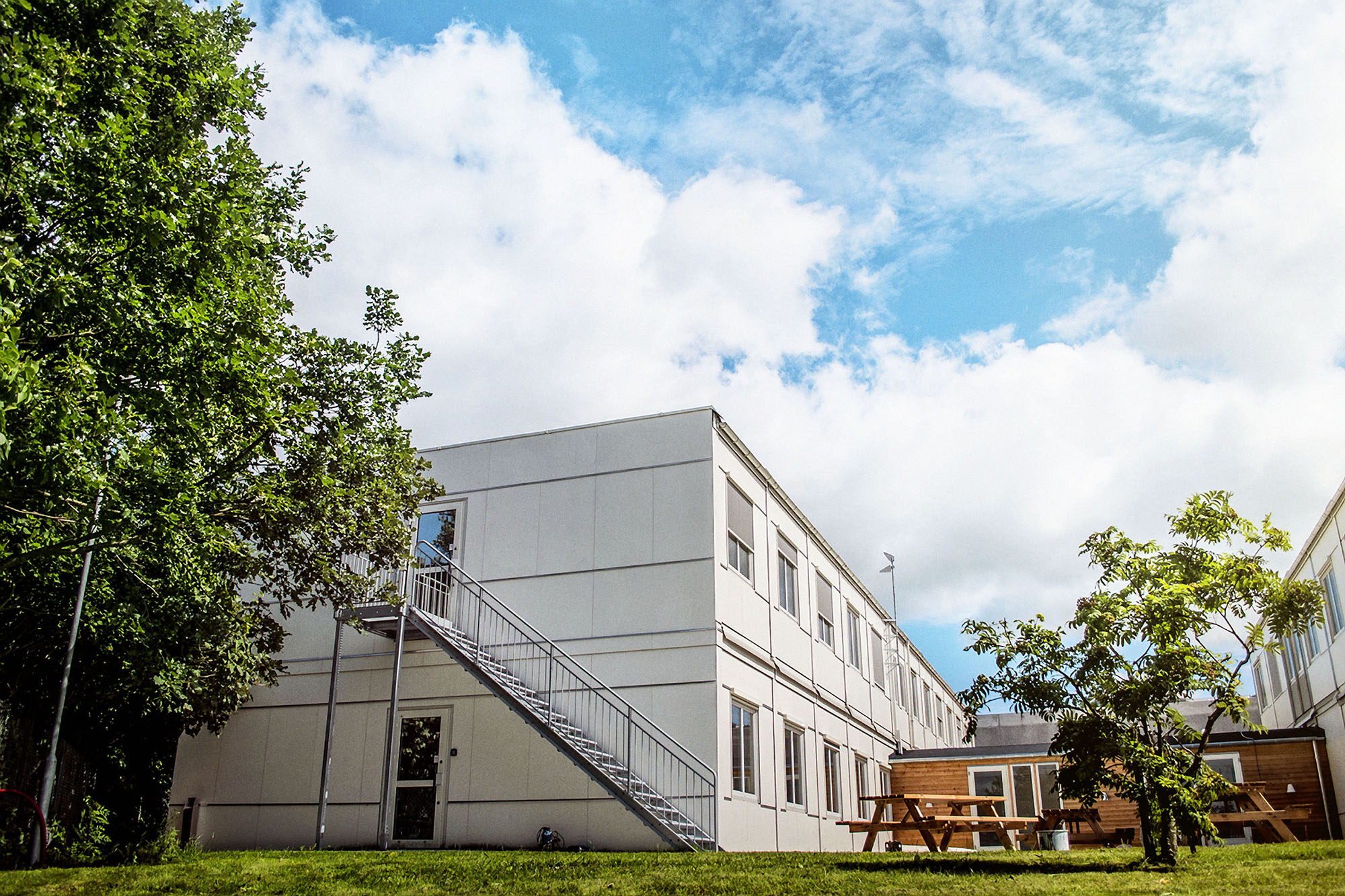 Vita kontorsmoduler i två plan placerade i grön utemiljö med träd och gräsytor. Flexibla kontorsmoduler från Expandia.