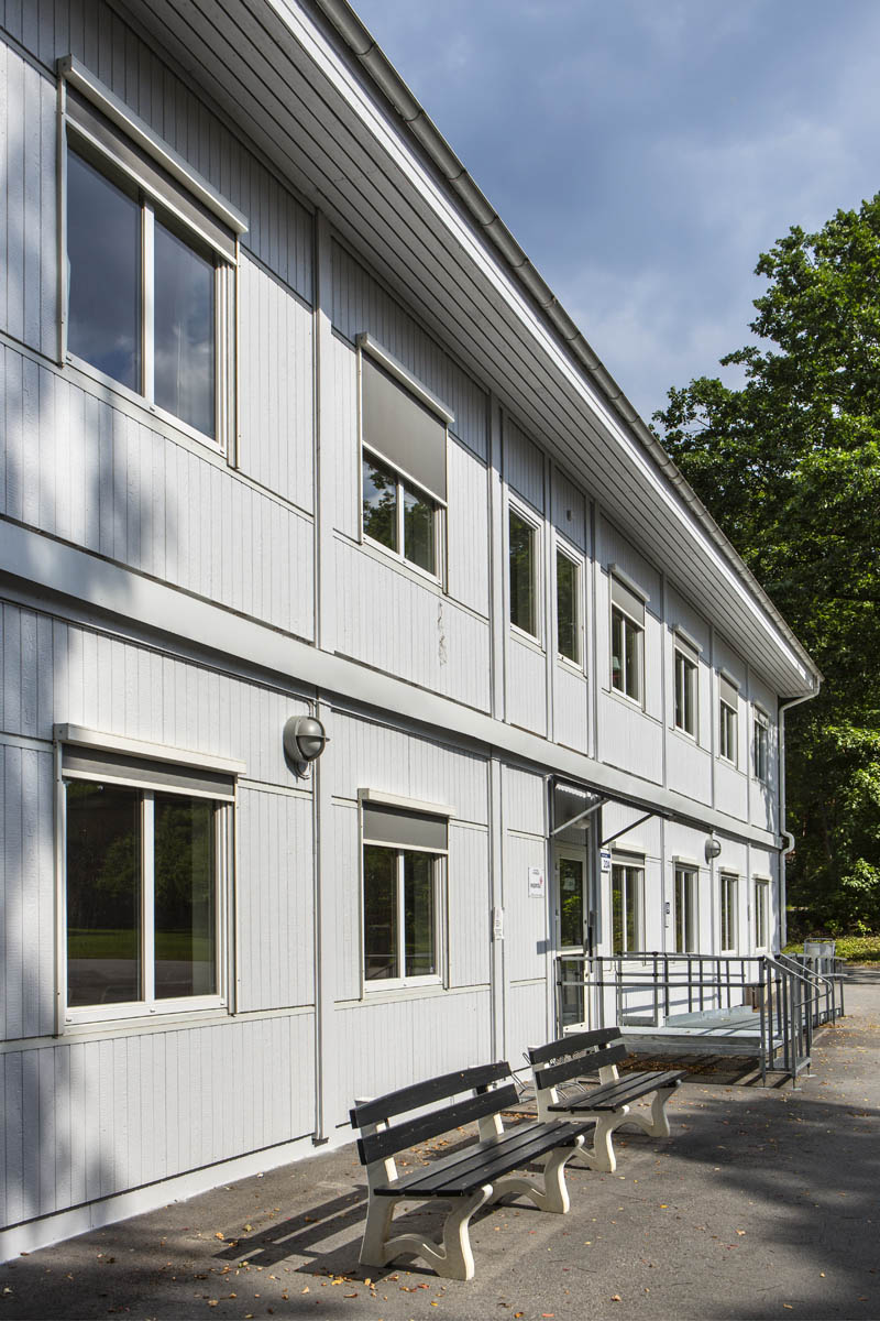 Ljusa kontorsmoduler i två plan med fönsterrader, entré med ramp och räcke, omgivna av grönska och träd i en lugn utemiljö – kontorsmoduler från Expandia.