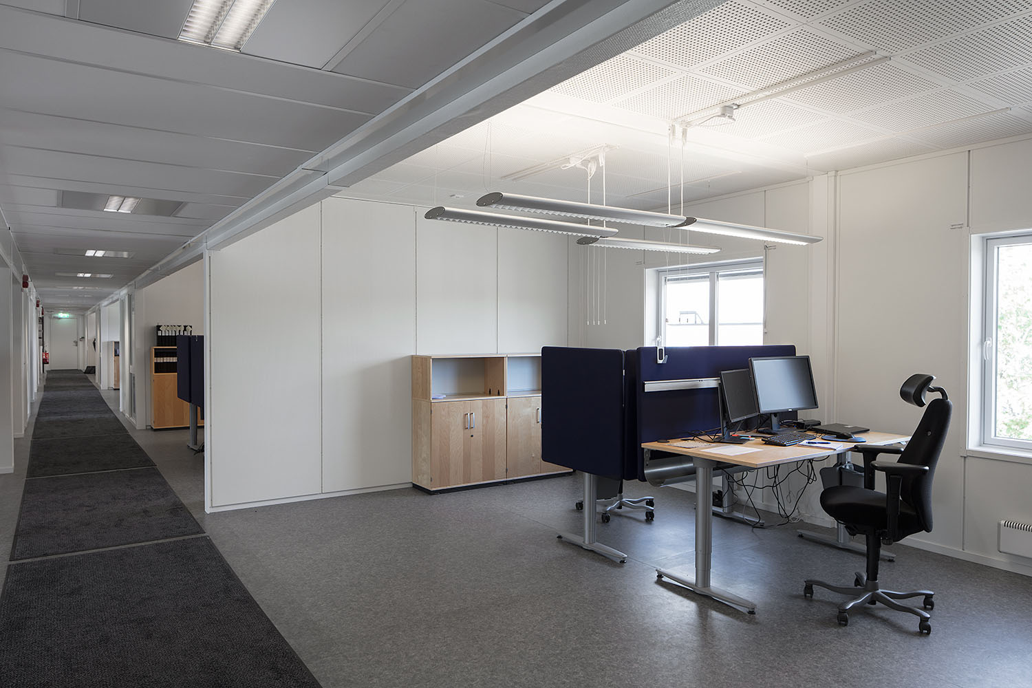 Ljust kontorslandskap med arbetsplatser, skrivbordsskärmar och korridor i bakgrunden, i moduler från Expandia.