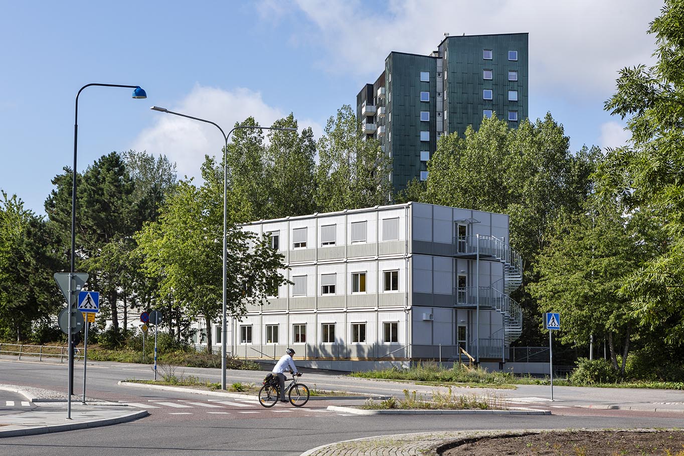 Tillfällig modulbyggnad från Expandia i tre våningar med kontorslokaler, placerad i grön stadsmiljö, med ljus fasad, många fönster och externa trappor.