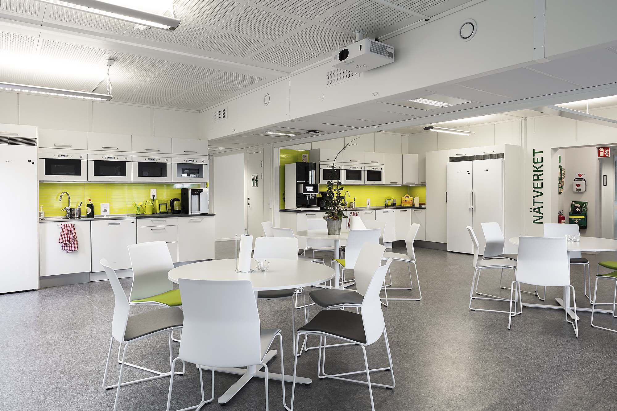 Landskrona Energi Ljust personalrum med köksdel, vita skåp och mikro­vågsugnar, kaffemaskiner, runda bord med vita stolar samt gröna detaljer på väggar och möbler