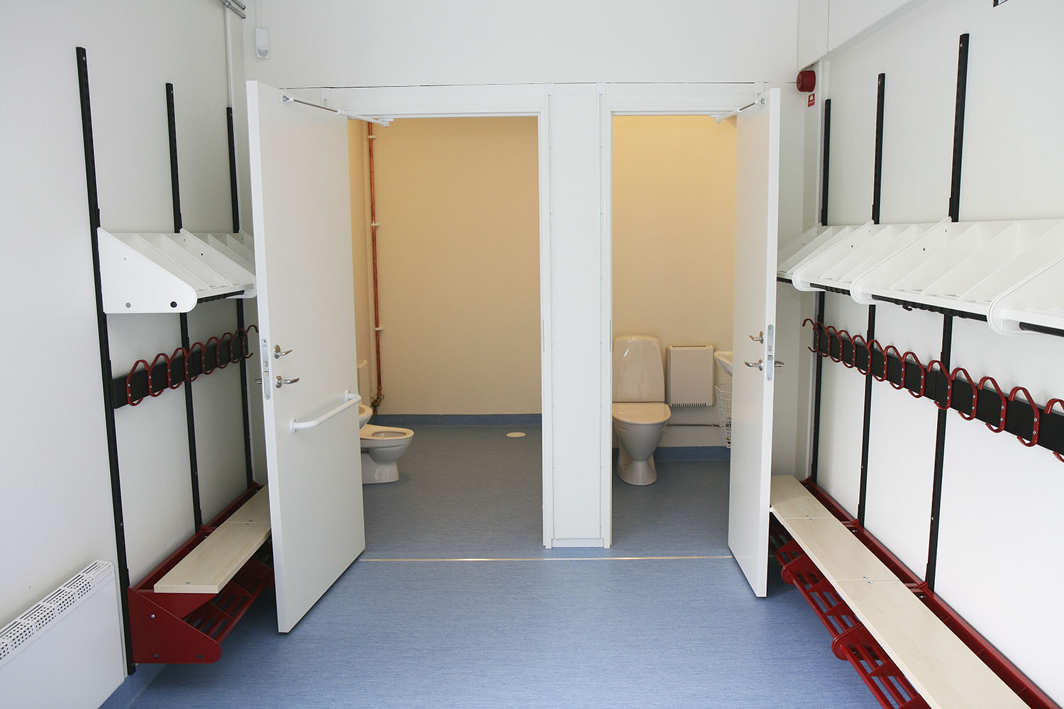 Omklädningsrum i skolmiljö med bänkar, krokar och två toaletter, placerat i en modullösning från Expandia anpassad för skolverksamhet.