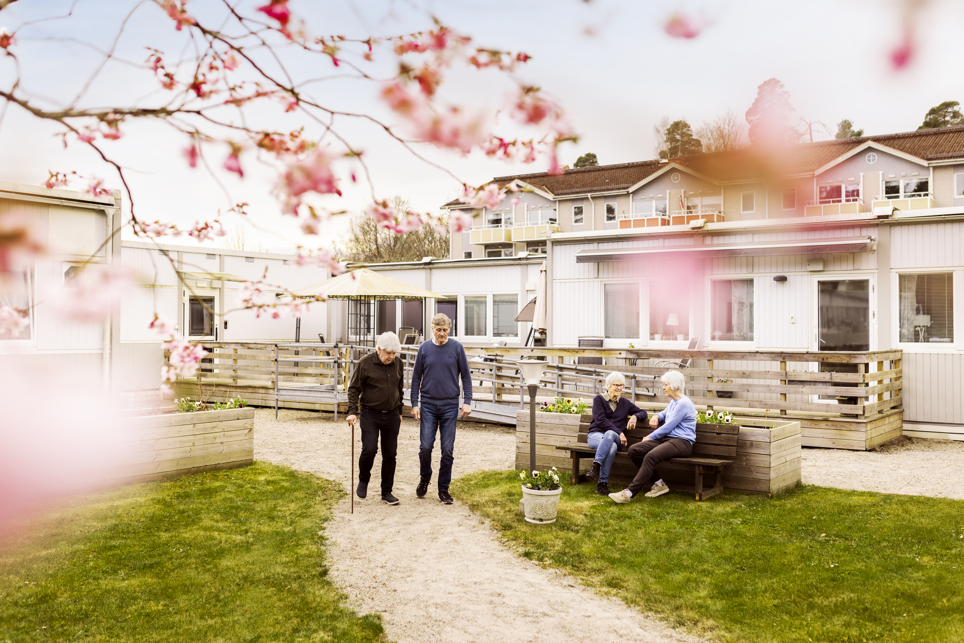 Innergård vid Borggården demensvård i Olofström där boende promenerar och sitter på bänkar i en grön utemiljö. I bakgrunden syns en modullösning från Expandia som ramar in gården.