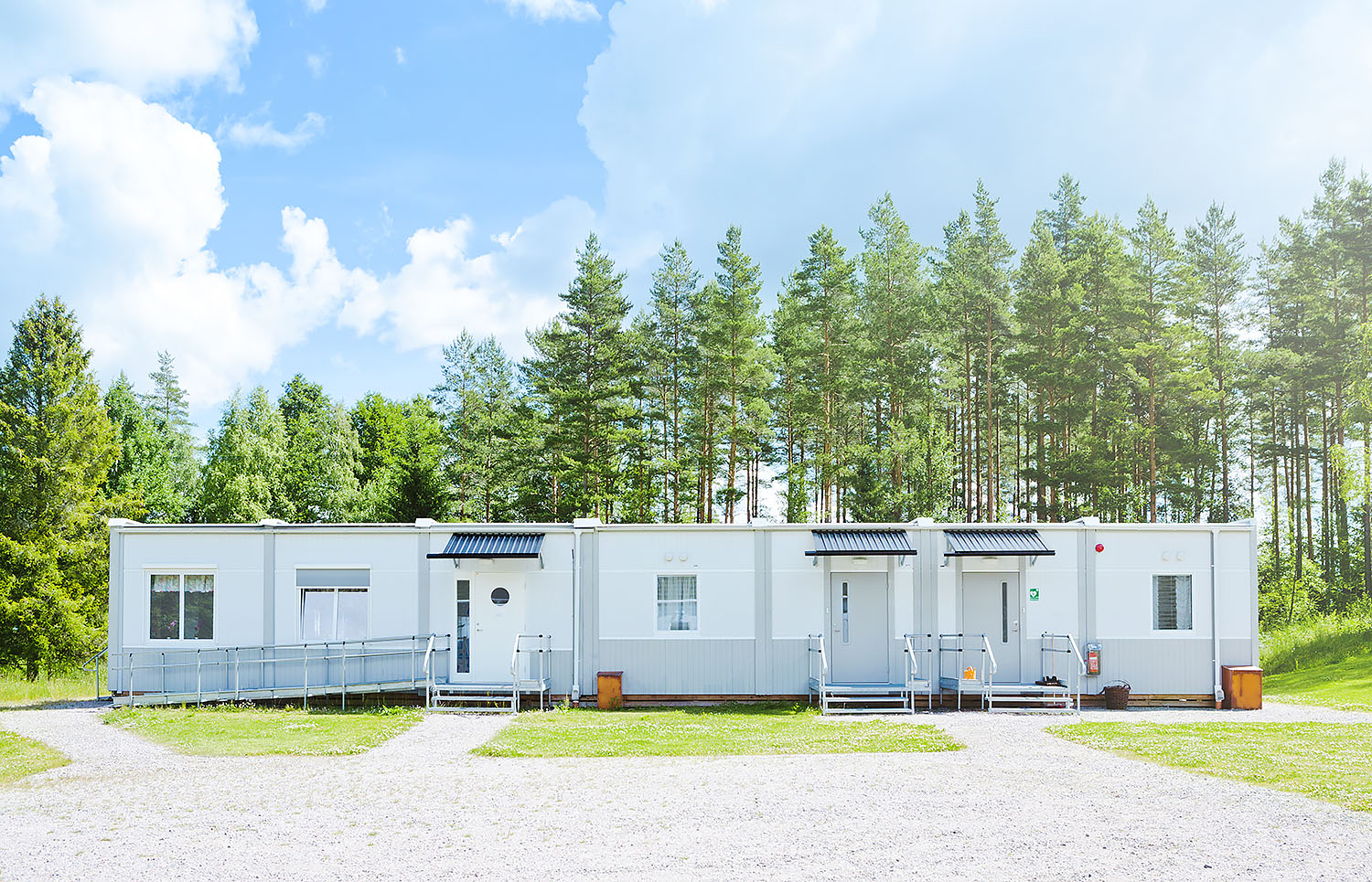 Vita boendemoduler från Expandia i Vingåker, placerade i grön miljö med träd i bakgrunden och entréer med ramper.