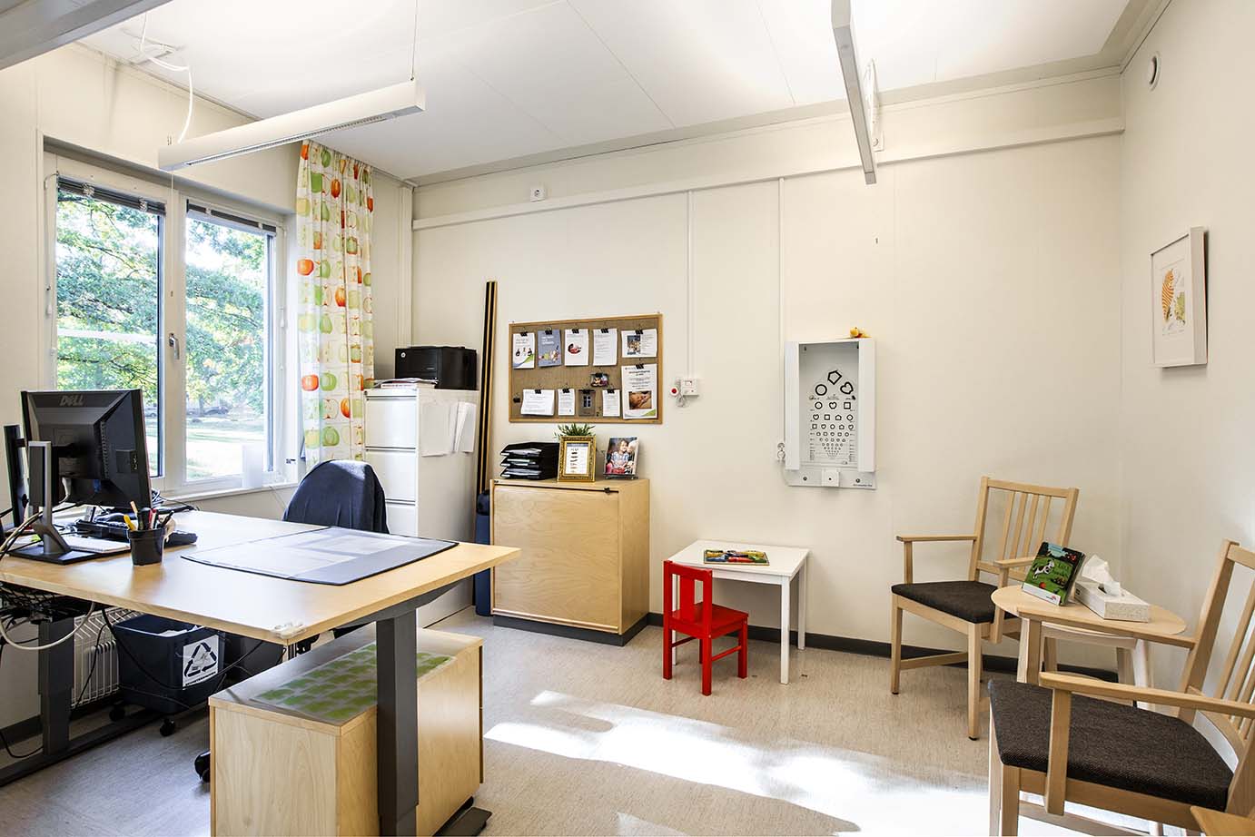 Ljust mottagningsrum i moduluppförd vårdlokal från Expandia med skrivbord, undersökningsutrustning, stolar och barnhörna vid fönster.