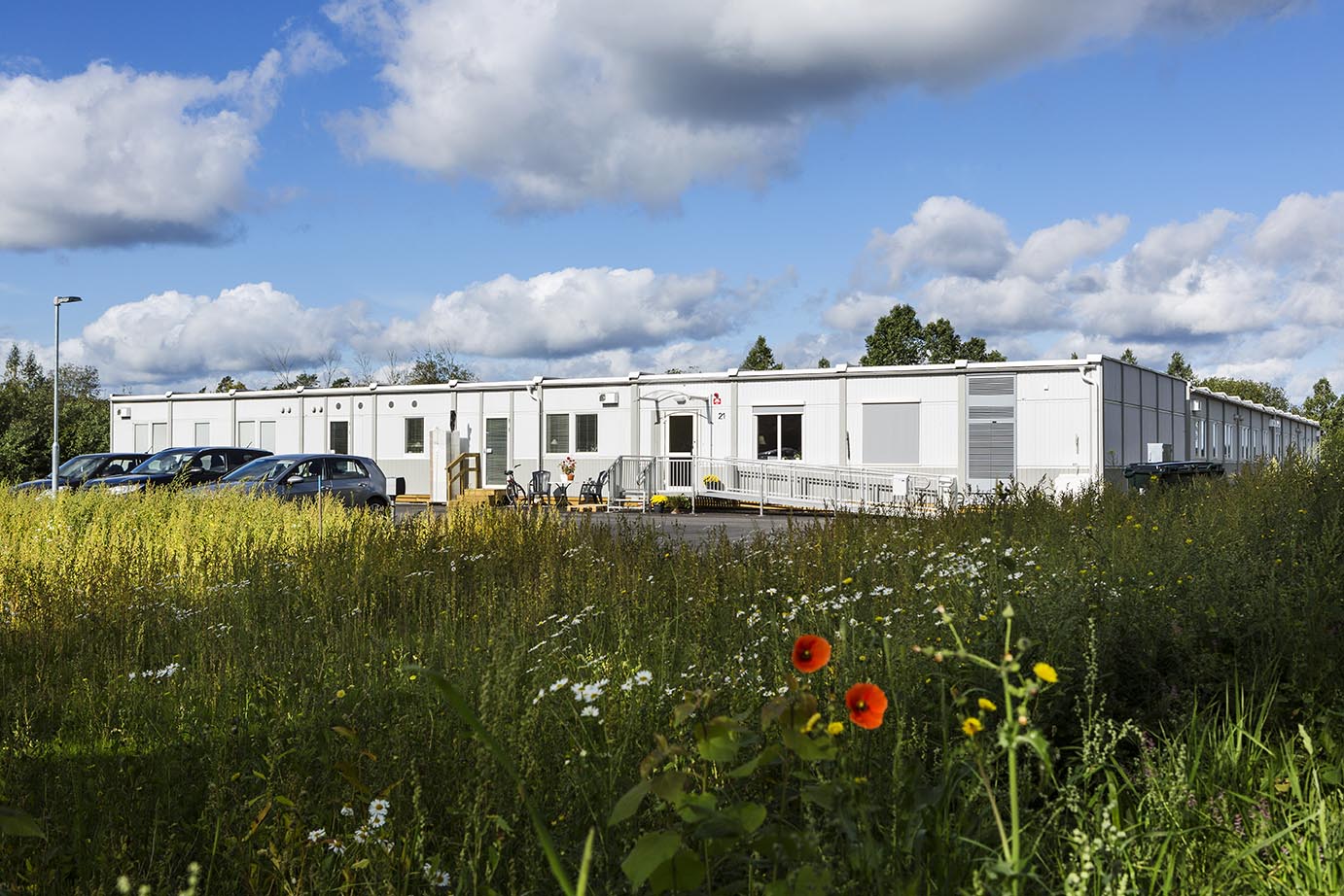 Nordrona LSS-boende i Norrtälje med vita boendemoduler från Expandia placerade i grön naturmiljö med ängsmark, träd och blå himmel.