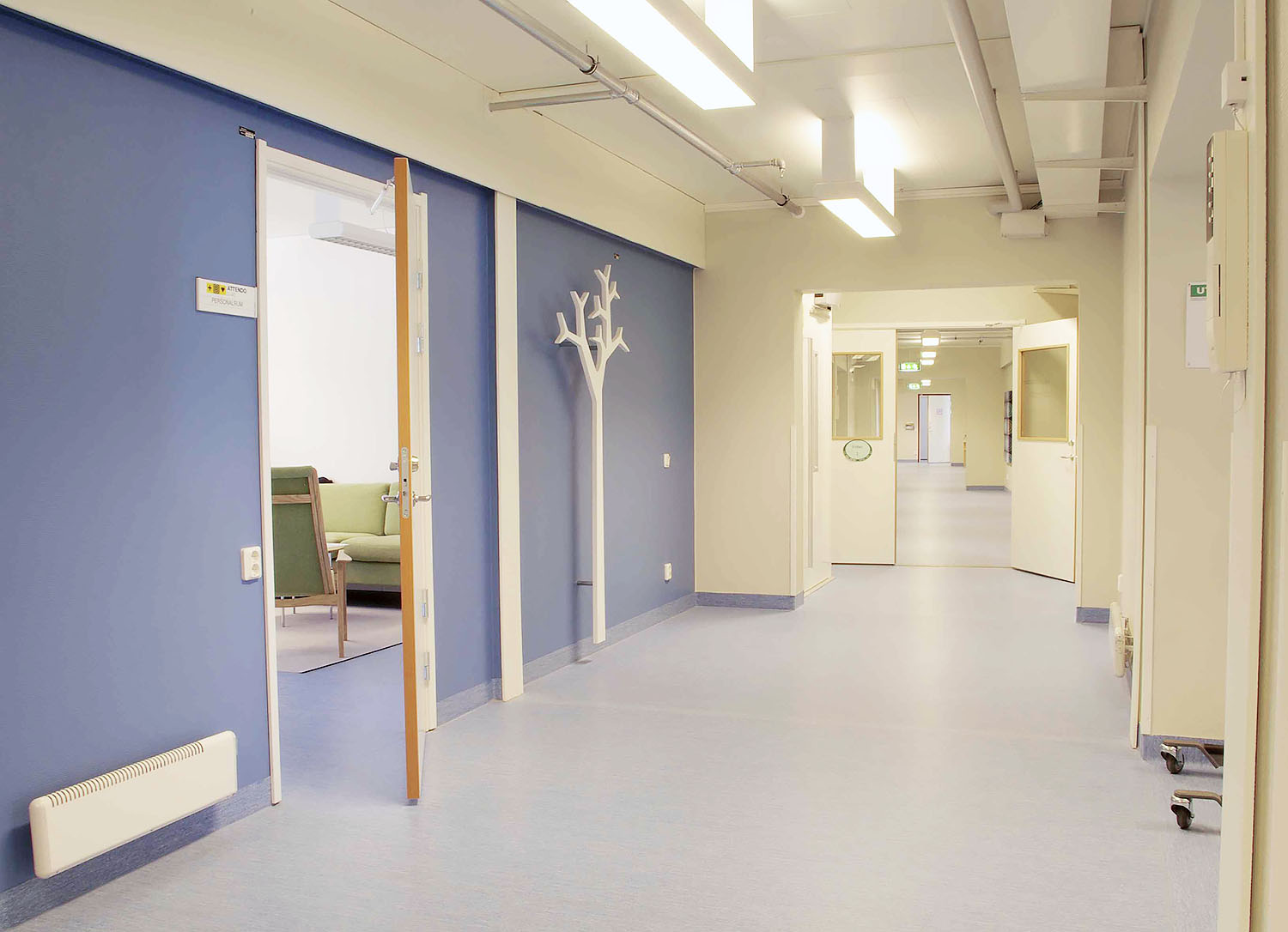 Ljus och rymlig korridor i boendemoduler från Expandia med blå väggar, öppna dörrar till gemensamma utrymmen och god tillgänglighet.